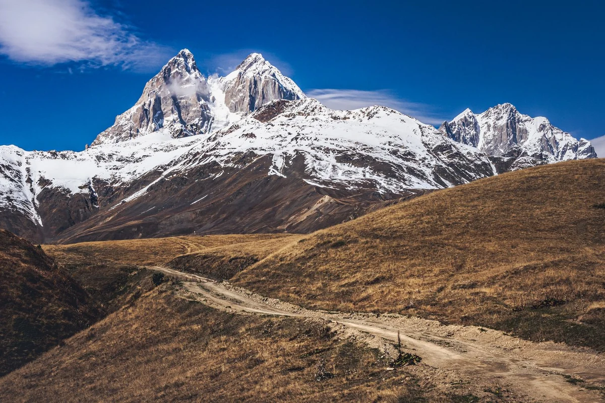 Dirt trail leading toward snow-capped Caucasus peaks above Mestia, Svaneti