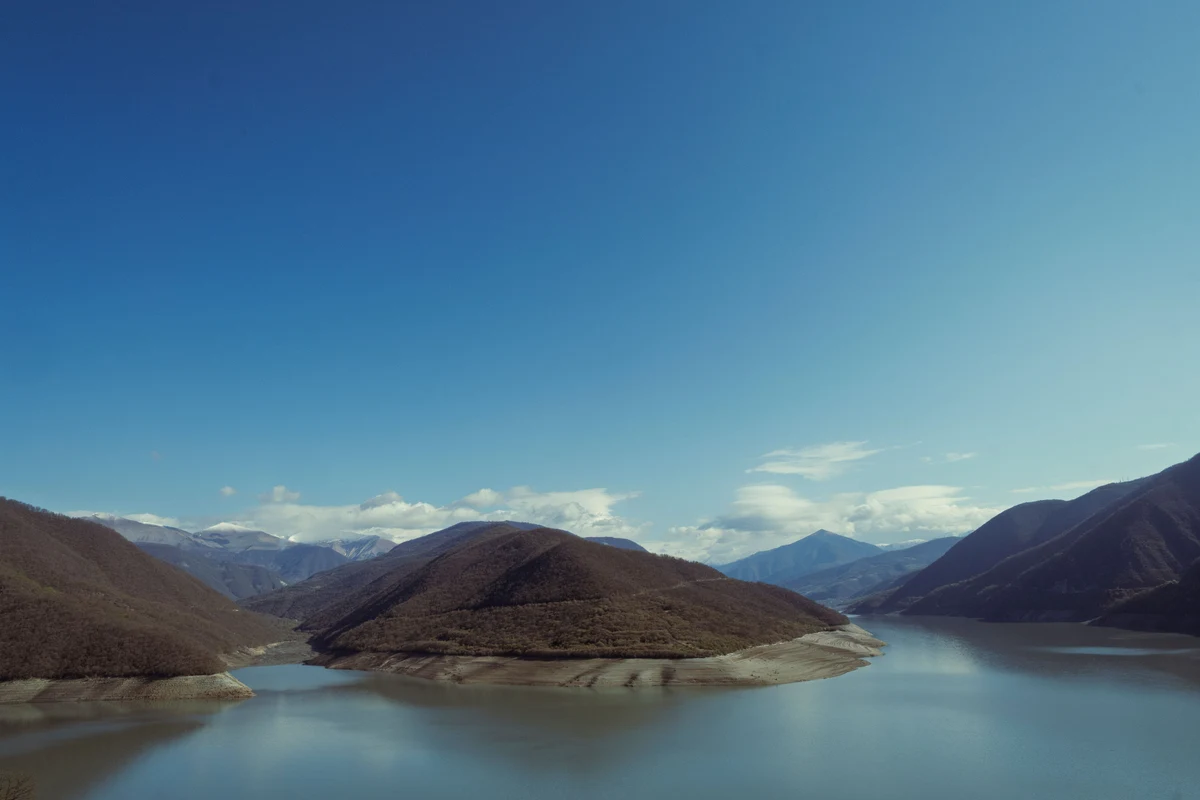 Peaceful mountain reservoir surrounded by forested slopes and snow-capped peaks in Georgia — the type of high-altitude lake scenery encountered on the Black Rock Lake trail in Lagodekhi National Park