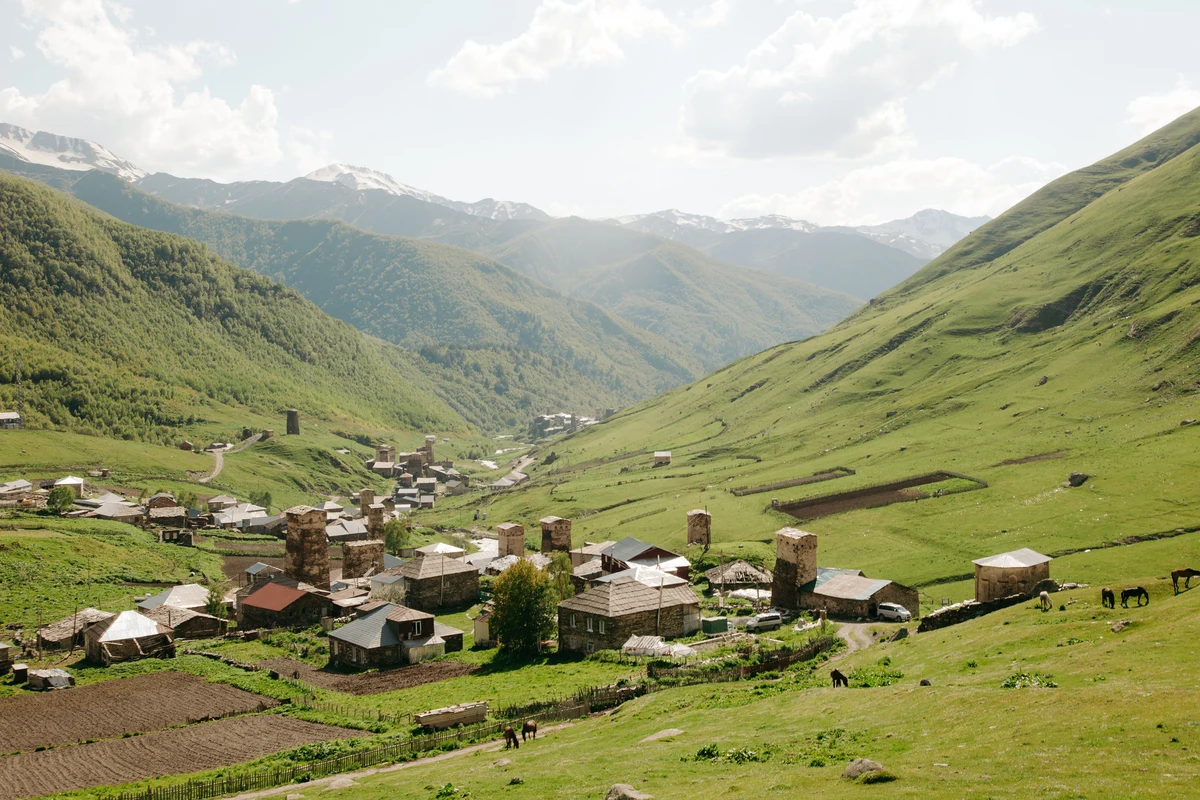 Traditional Georgian highland village nestled in a lush green valley with towering mountain peaks — typical settlement encountered on the Omalo to Shatili trekking route